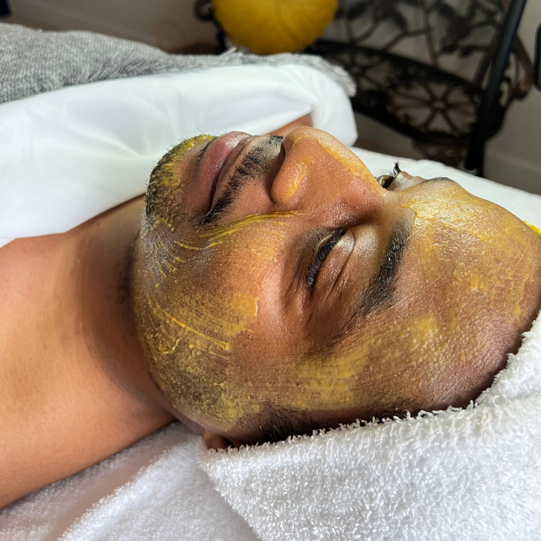 Hands of masseuse applying mud mask on african woman back. Young african american girl relaxing with eyes closed while beautician applying exfoliation clay on shoulder. Woman at resort doing clay mask exfoliation.